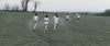 Cross-country runners crossing a misty green field — grainy 16mm documentary film clip